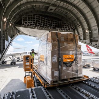 Wrapped pallet of freight being loaded into an aircraft. | Shipping to PNG